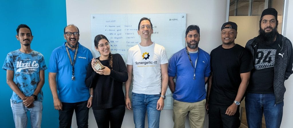 Sieben Bootcamp-Teilnehmer und ihr Trainer stehen für ein Teamfoto nebeneinander vor einem Whiteboard.
