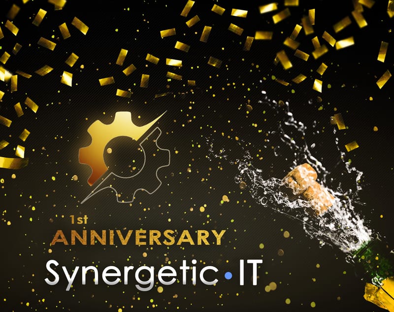A bottle of champagne being uncorked among golden confetti, beside a golden Synergetic IT logo celebrating the company's first anniversary.